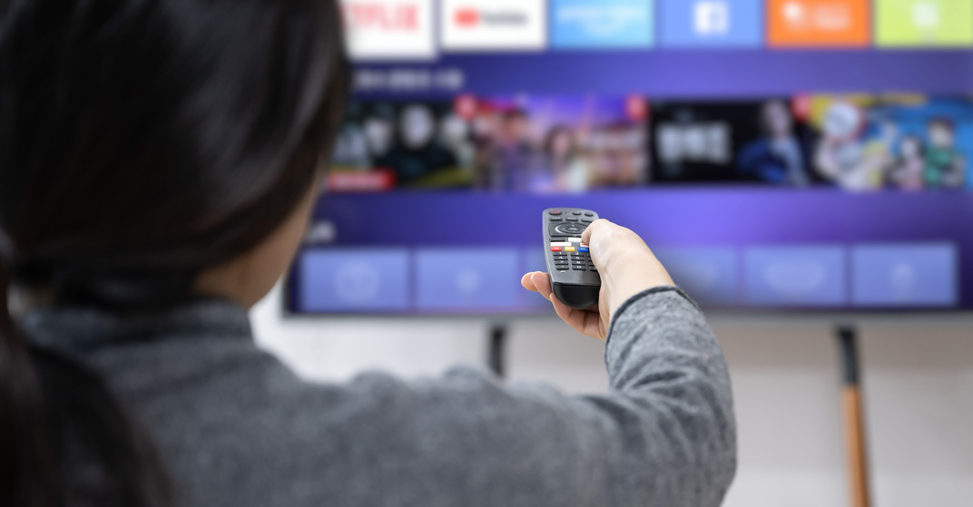 Eine dunkelhaarige Frau wählt mit der Fernbedienung eine Streaming-App auf Ihrem Smart-TV aus