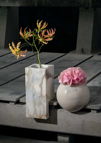zwei Edgy-Vasen von Breitwieser an dunklem Holztisch, länglich, aus buntem Marmor mit Trockenblumen drin, einmal klein, rund und hellgrau mit rosa Blumen