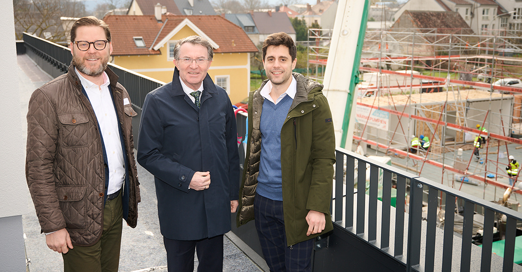 Lukas Schermann, Rafael Lughammer und Franz Piribauer stehen nebeneinander auf einem Balkon, im Hintergrund eine Baustelle und ein dunkles Geländer