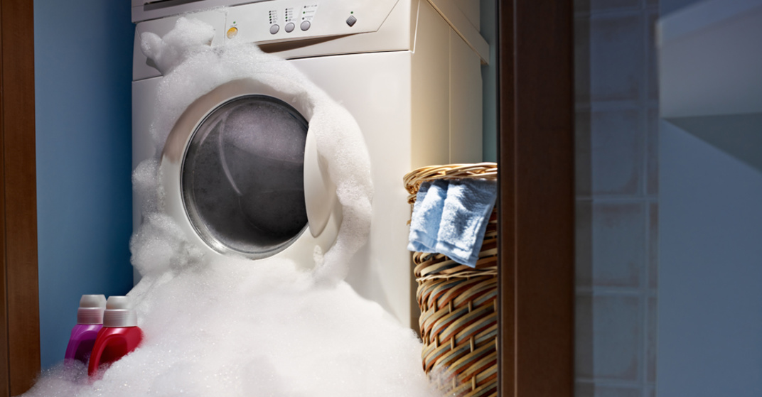 Wasserschaden! Waschmaschine in Waschküche, aus der dicke Schichten Schaum und Wasser quellen