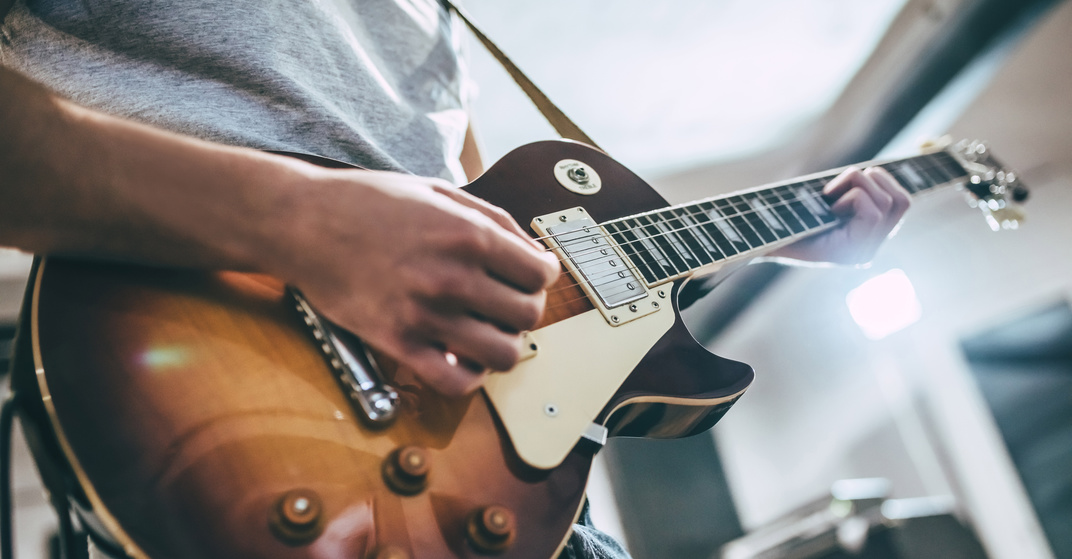Junger Mann in grauem Shirt spielt braun-beige E-Gitarre. Großaufaufnahme, Gesicht nicht zu sehen